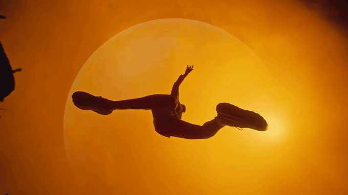 A runner leaps in silhouette across a giant golden moon in an amber sky