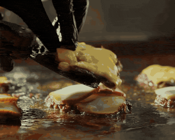Gloved hands stack cheese-topped patties on a glistening griddle, then the finished burger in close-up