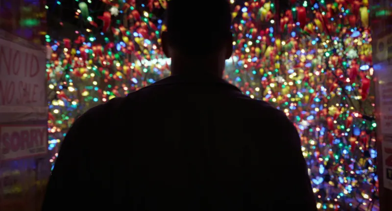 A figure in silhouette in front of a wall of coloured fairy lights, from Birdman