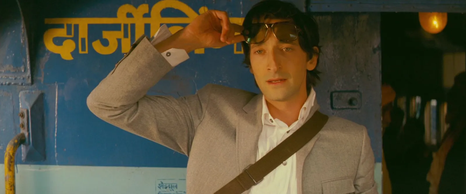 A man leans out of a bright blue train under a hand-painted yellow sign, from The Darjeeling Limited