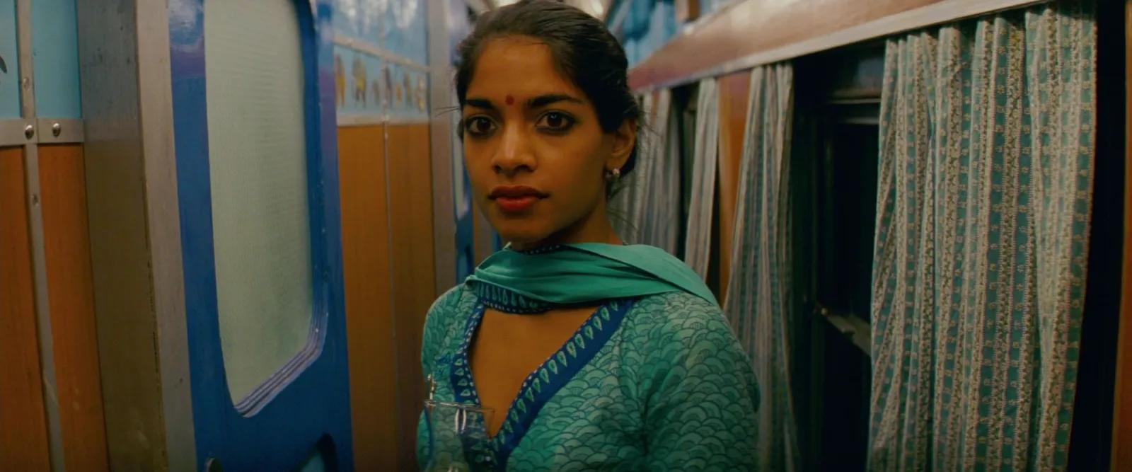 A woman in a teal sari at a train window, teal and blue tones