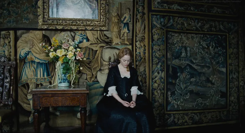 A young woman in black sits small against walls of blue-green tapestries in soft window light, from The Favourite