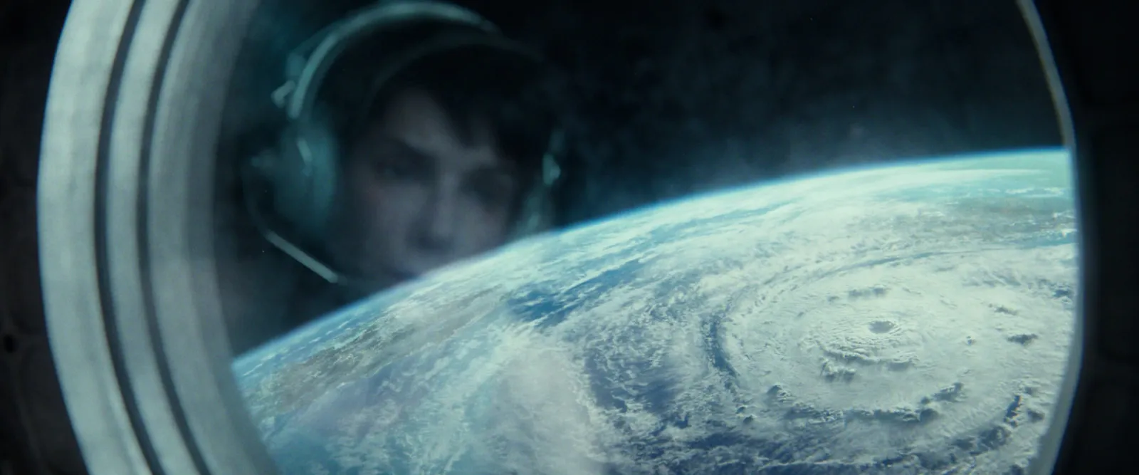 A face inside a helmet seen through a round porthole, a hurricane over the Earth below
