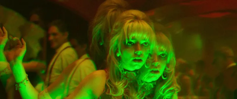 Two blonde women with 1960s beehives side by side in a nightclub crowd, washed in acid green light, from Last Night in Soho