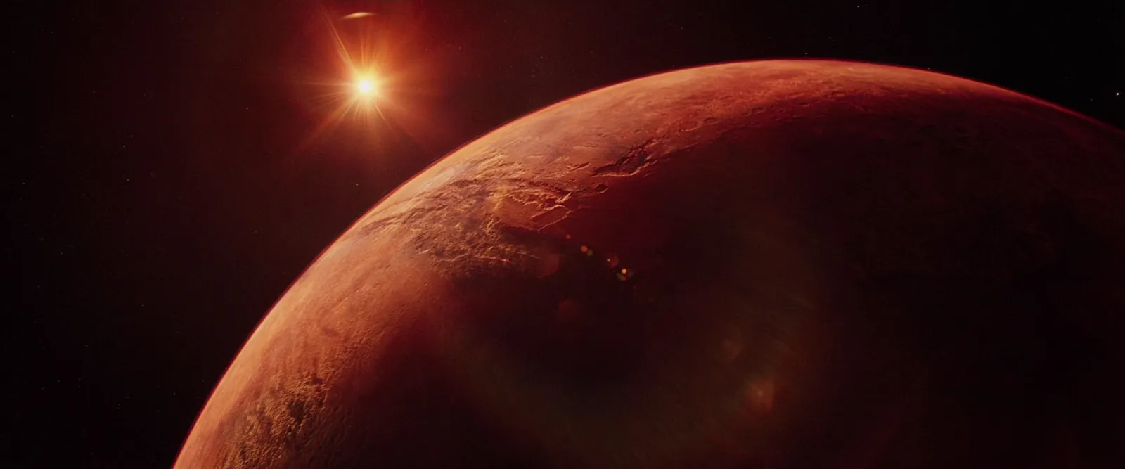 A rust-red planet under a small, hard sun in black space
