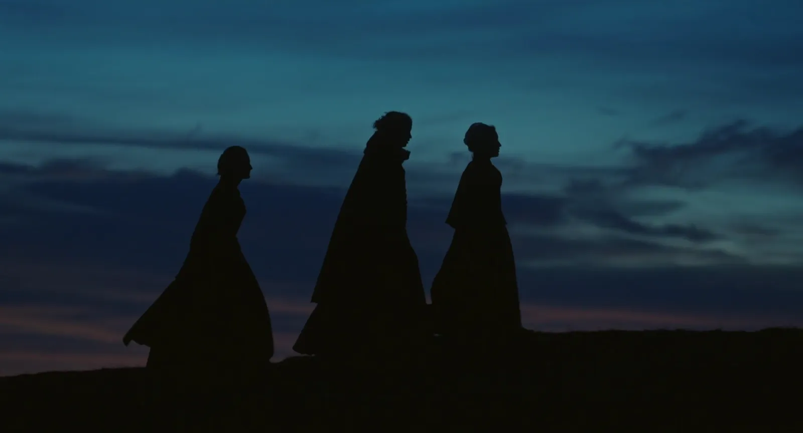 Three cloaked silhouettes standing against a deep blue dusk sky