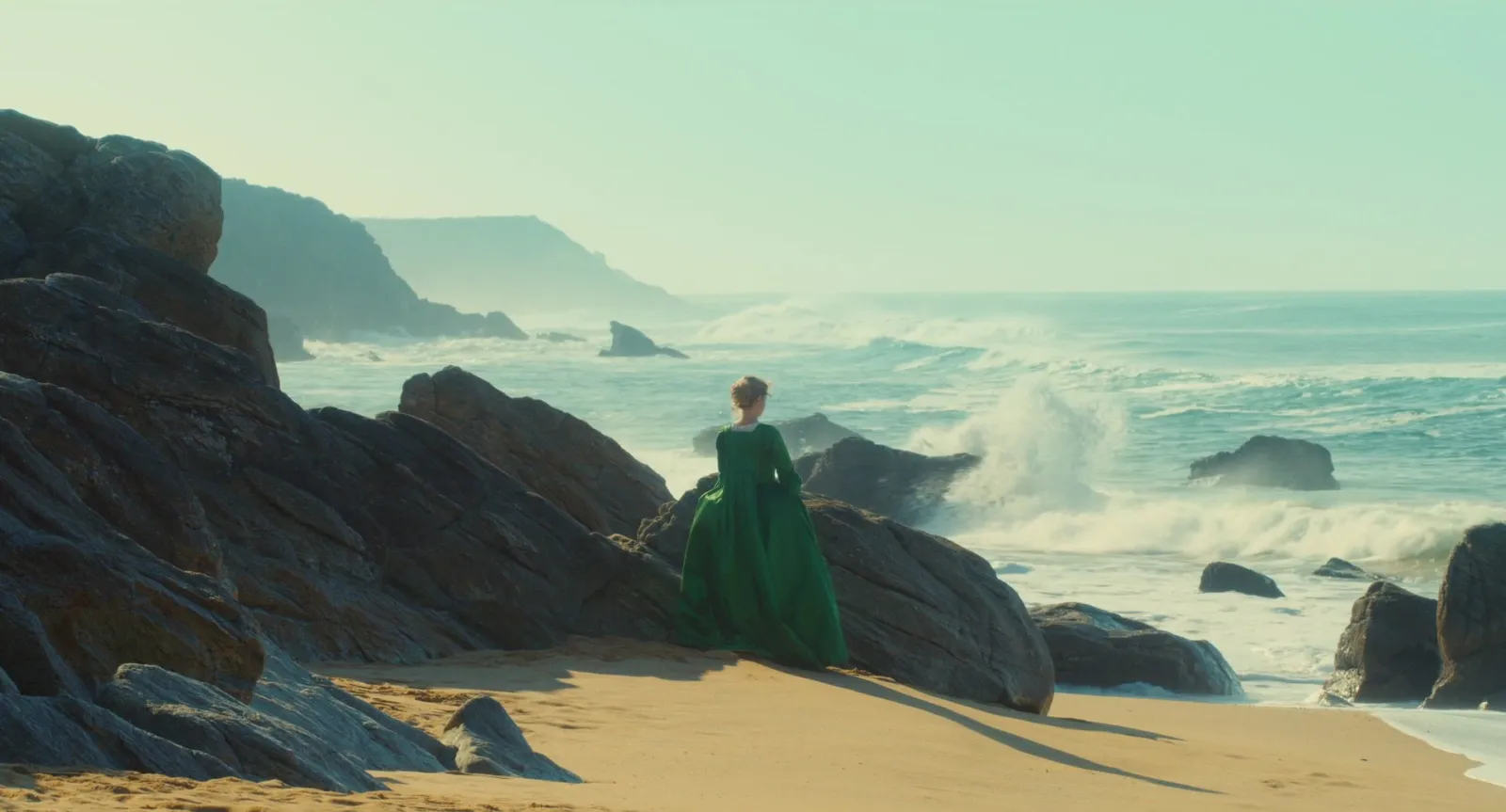 A woman in a green dress on a rocky shore, waves breaking