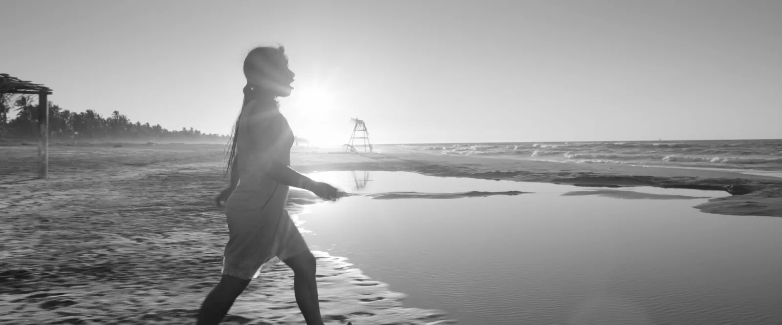 A woman walking along a beach into the sun, black and white