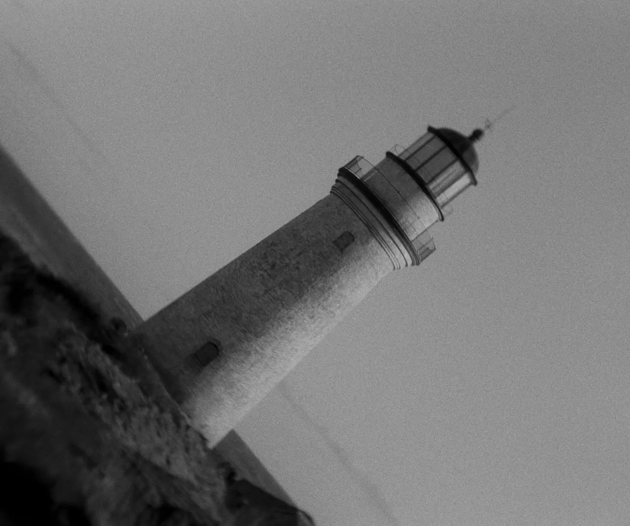 The lighthouse tower at a tilted angle, in black and white
