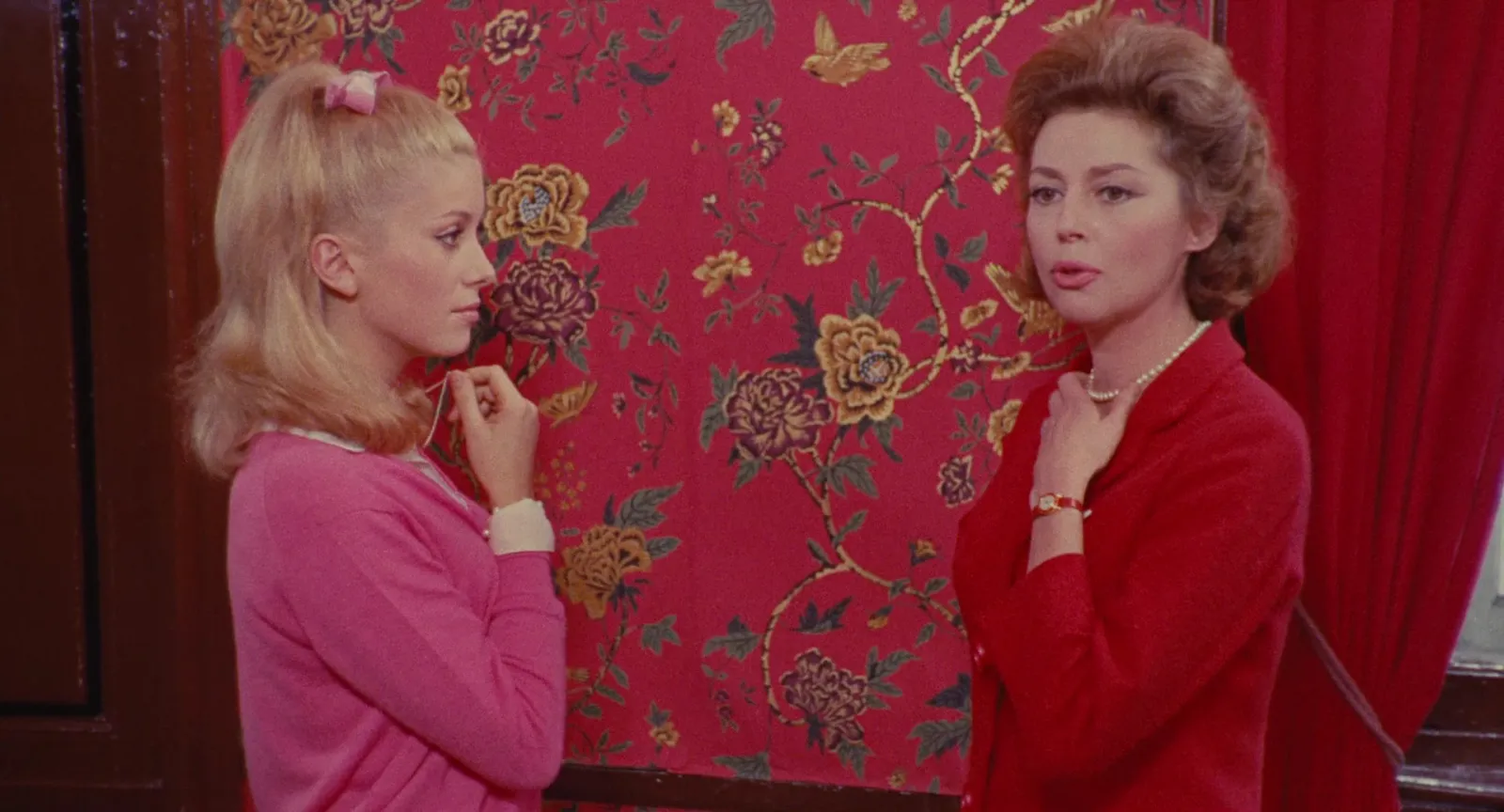 Two women in pink and red against red floral wallpaper
