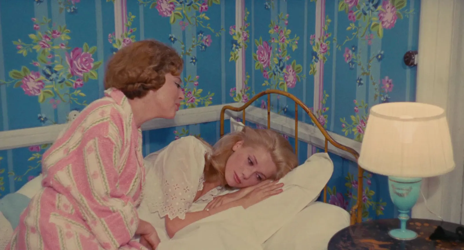 A bedroom with blue floral wallpaper and pink bedding